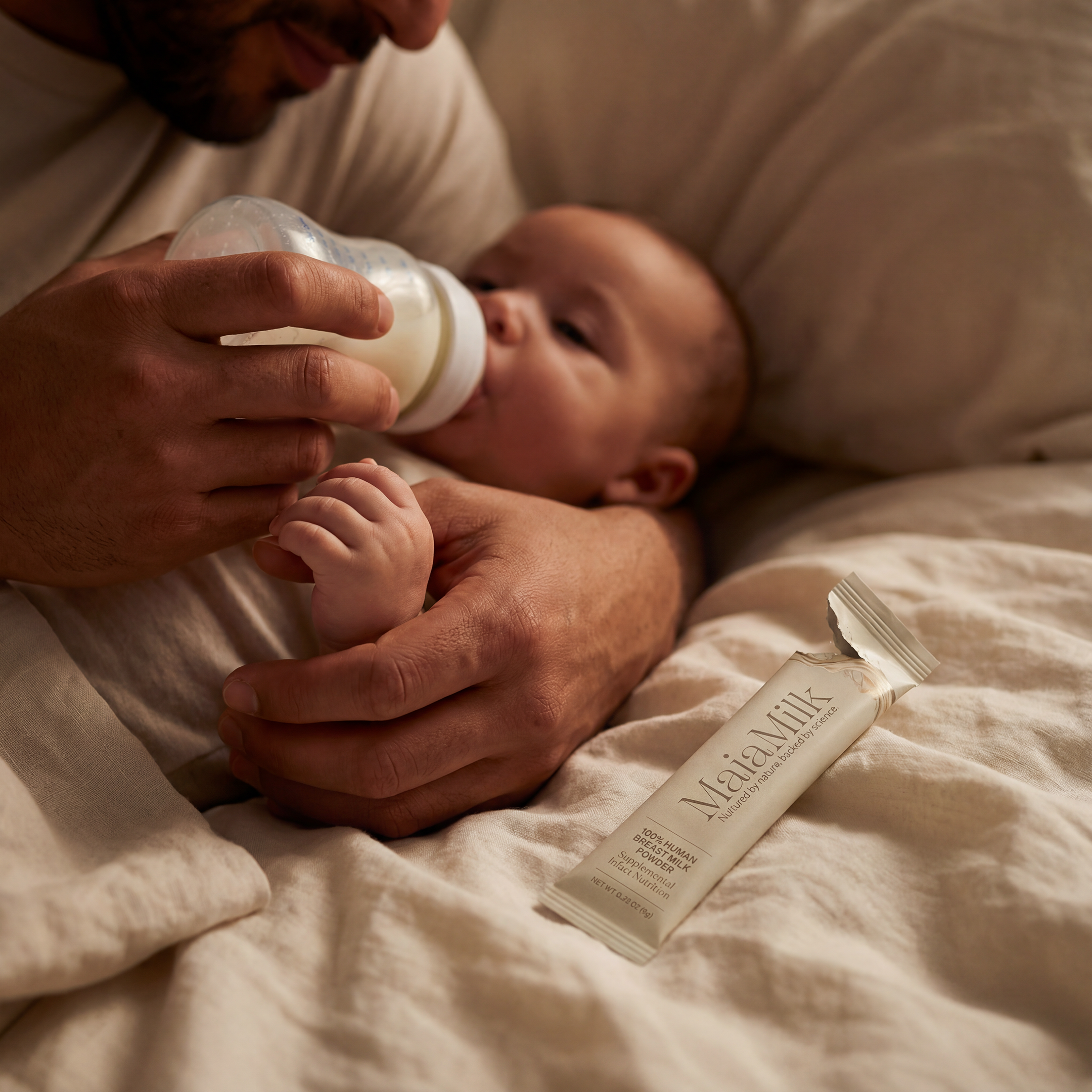 Baby being fed from a bottle with a MaiaMilk package on a bed