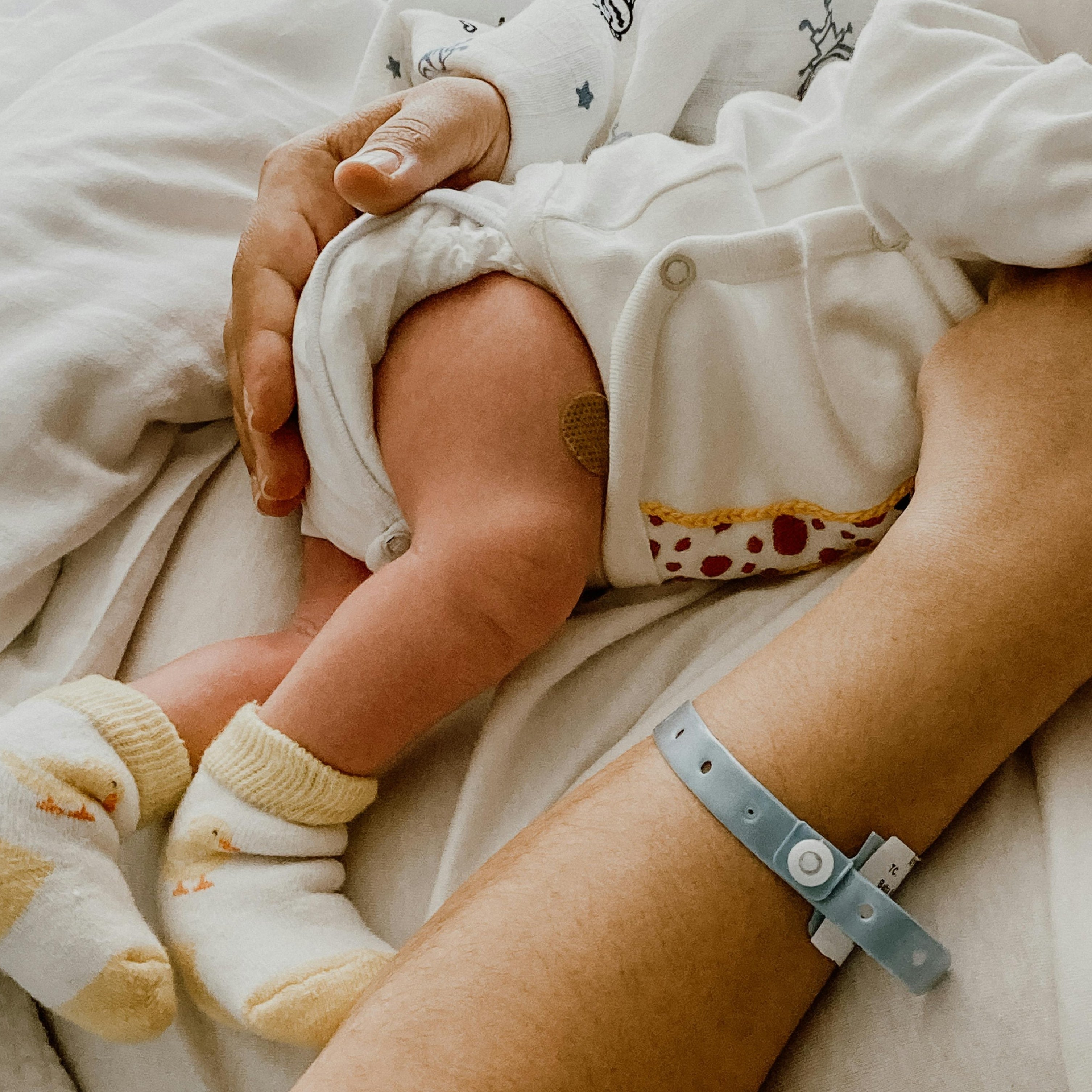 Baby in white outfit with star pattern held by an adult on a bed.